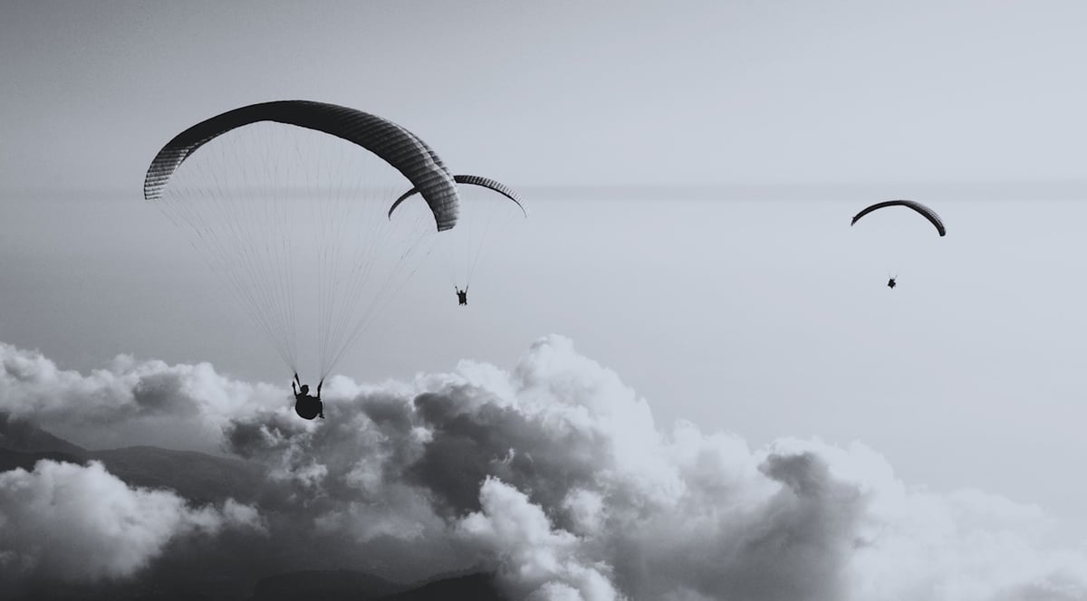 Tre paragliders ovanför ett tjockt molntäcke