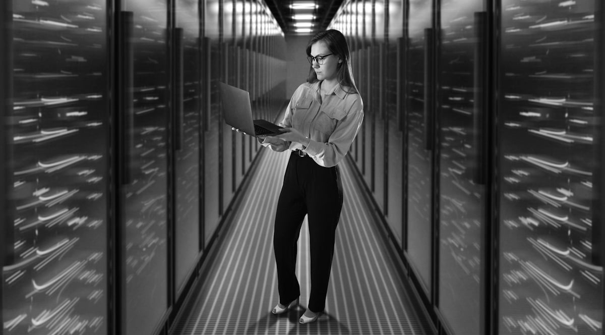 Kvinna med bärbar dator stående i en lysande 3D-serverkörridor. 