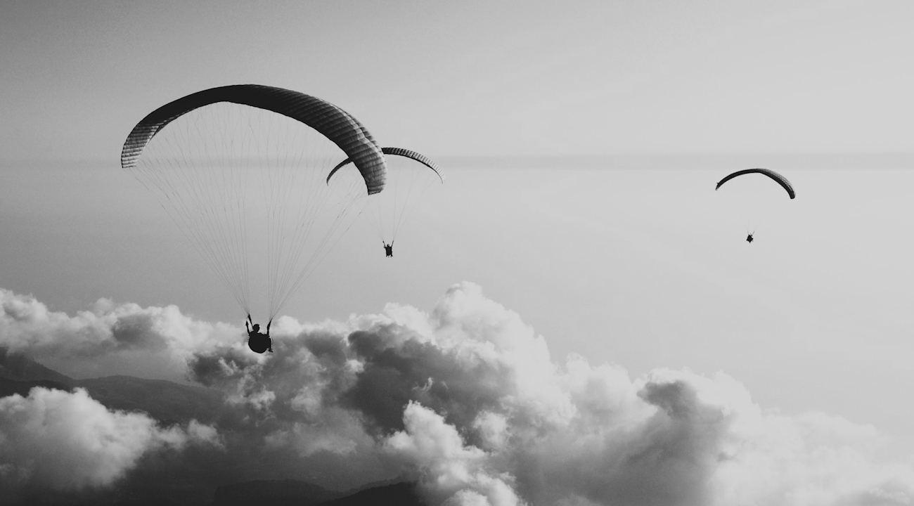 Tre paragliders ovanför ett tjockt molntäcke