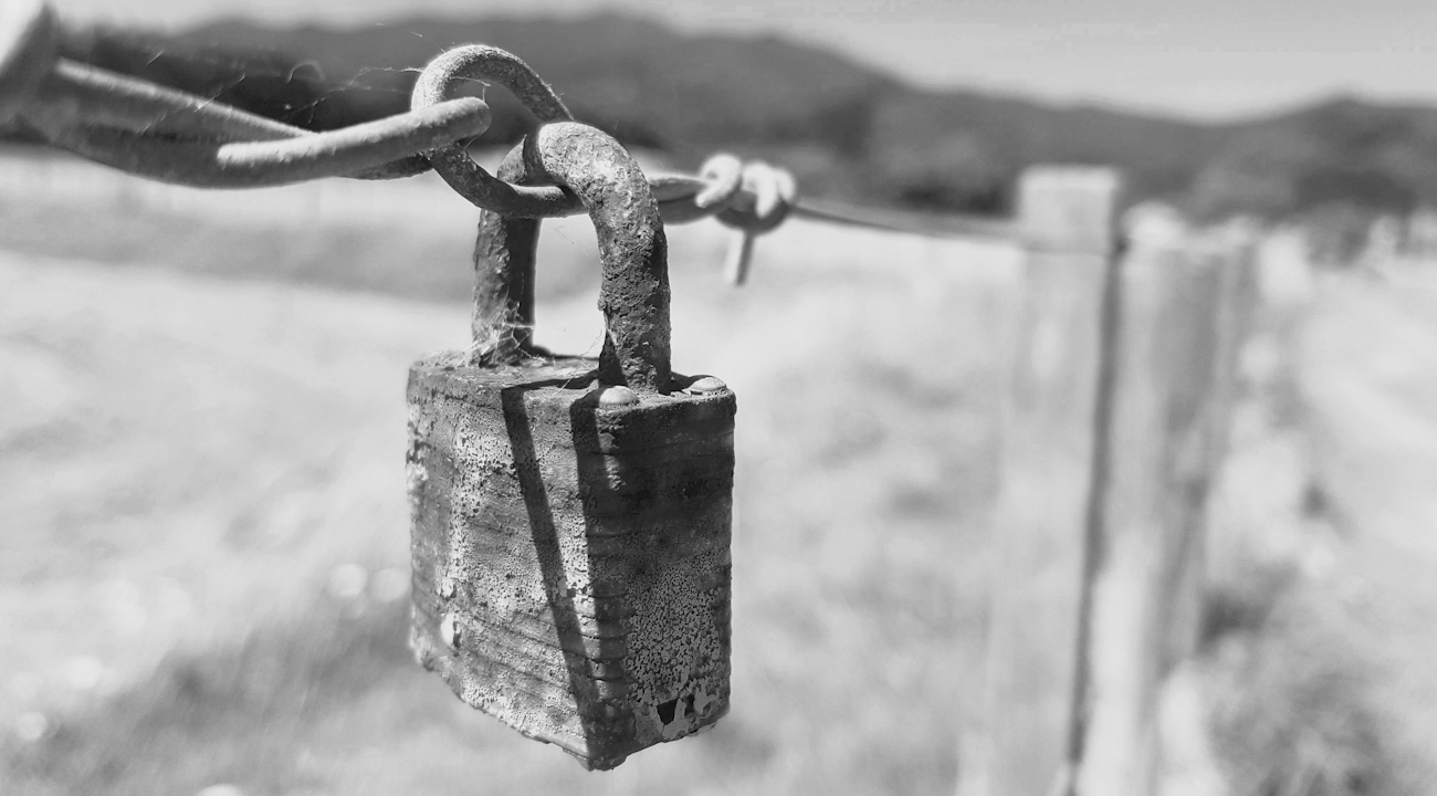 Rostigt hänglås som hänger på ett staket